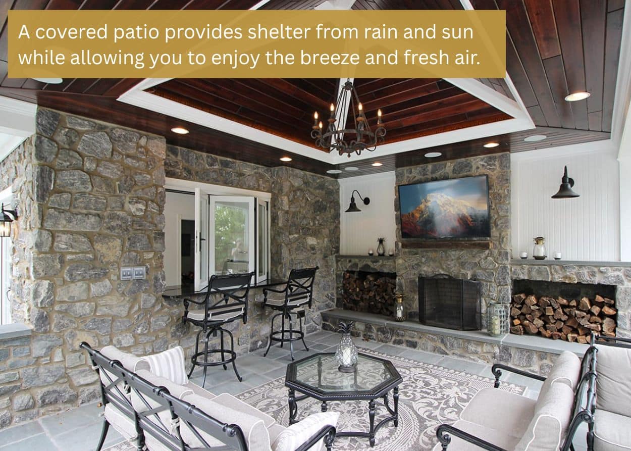 Elegant covered patio with stone walls, dark wood ceiling, chandelier, built-in bar seating, and a fireplace. Caption: A covered patio provides shelter from rain and sun while allowing you to enjoy the breeze and fresh air.